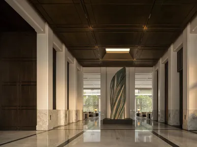 Symmetrical view of a modern luxury hotel lobby with polished marble floors, dark wood paneling, coffered ceiling with skylight, and a tall twisted bronze sculpture in the center.