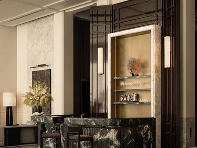 Elegant hotel lobby interior with a curved green marble reception desk, two bar stools, dark wood paneling, and a built-in back bar with glassware and decorative coral.
