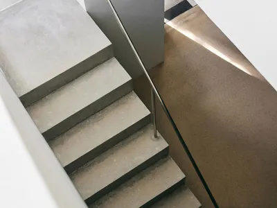 High-angle view of a minimalist concrete staircase with stainless steel handrail and dramatic natural light casting long shadows on the lower landing.