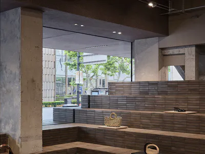 Modern retail interior featuring tiered wooden display steps against raw concrete walls, with clothing and woven bags displayed under industrial track lighting.