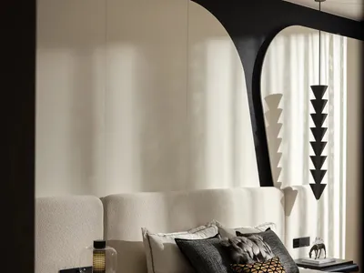 Modern luxury bedroom with a cream boucle upholstered headboard, black sculptural arch wall feature, black pendant light with stacked conical shades, and animal print throw blanket on the bed.