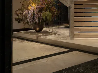 Modern luxury hotel lobby featuring a grand marble staircase with integrated lighting and a large sculptural floral arrangement in a bronze vase on a marble platform.
