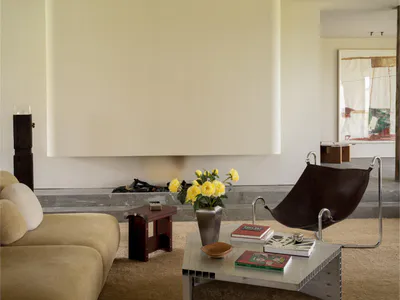 極簡風客廳，米色布沙發、咖啡色皮革吊椅、金屬茶几、大理石壁爐與黃玫瑰花瓶。
