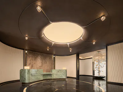 Luxurious hotel lobby featuring a curved green marble reception desk, dark reflective marble floor with gold inlay, and a dramatic circular ceiling fixture with integrated lighting and crystal accents.