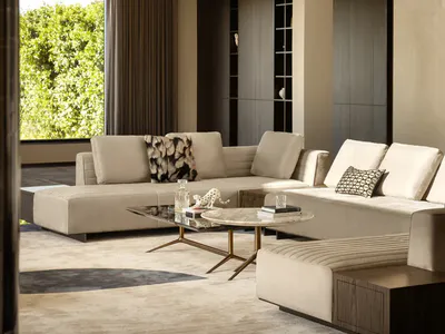 Modern luxury living room with a large beige sectional sofa, marble and glass coffee tables, sculptural brass pendant light, and large window overlooking green foliage.