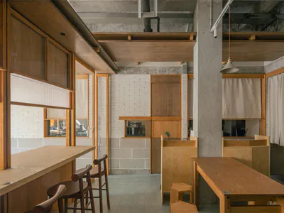 台灣工業風咖啡廳室內，展現外露清水模天花板、橡木長桌與吧台、木椅，以及白磚牆面。