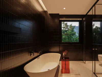 Modern dark-themed bathroom interior with a white freestanding bathtub, black rectangular wall tiles, glass-enclosed shower and toilet area, and a small red side table with flowers next to a large window overlooking green trees and buildings.