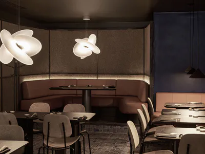 Modern Japanese-inspired restaurant interior featuring curved brown leather banquettes, dark textured walls, sculptural white flower-shaped pendant lights, and neatly set dining tables with grey upholstered chairs.