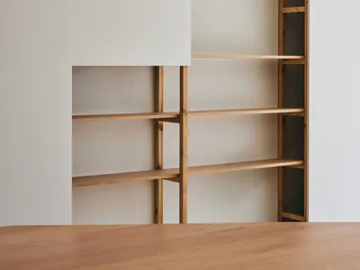 Modern minimalist living room featuring custom light oak built-in shelving units recessed into a white wall, with a solid oak table in the foreground.