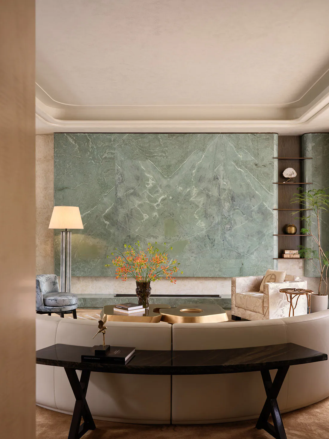 Modern luxury living room featuring a large green marble wall, curved cream sofa, brass coffee tables, and built-in shelving.