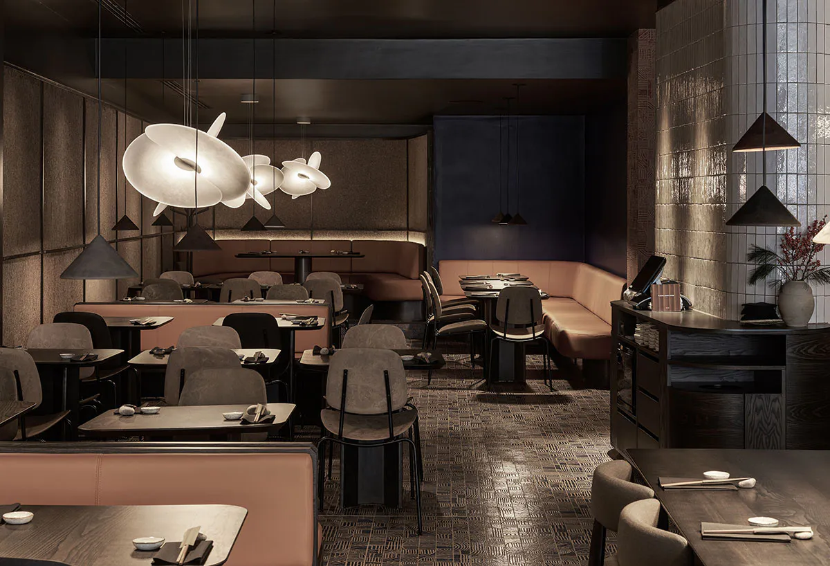 Modern Japanese restaurant interior with dark walnut tables, blush pink banquettes, sculptural white pendant lights, and textured walls.