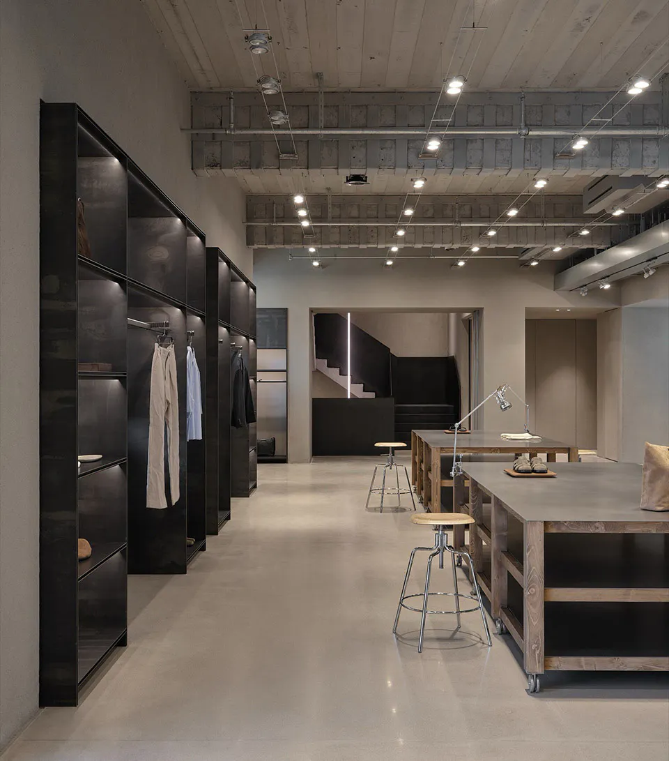 Modern industrial minimalist dressing room with black steel open wardrobes, concrete floor, wooden work tables on wheels, and exposed ceiling infrastructure.
