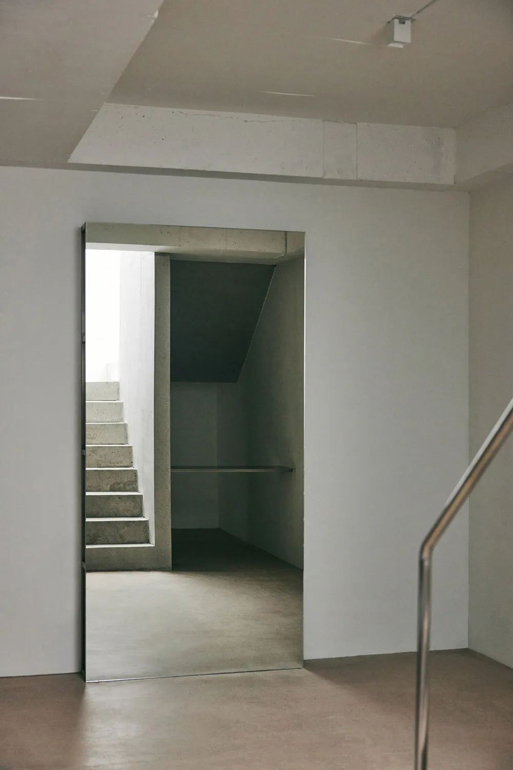 View of a minimalist concrete staircase and hallway with exposed concrete walls and floor in a modern interior.
