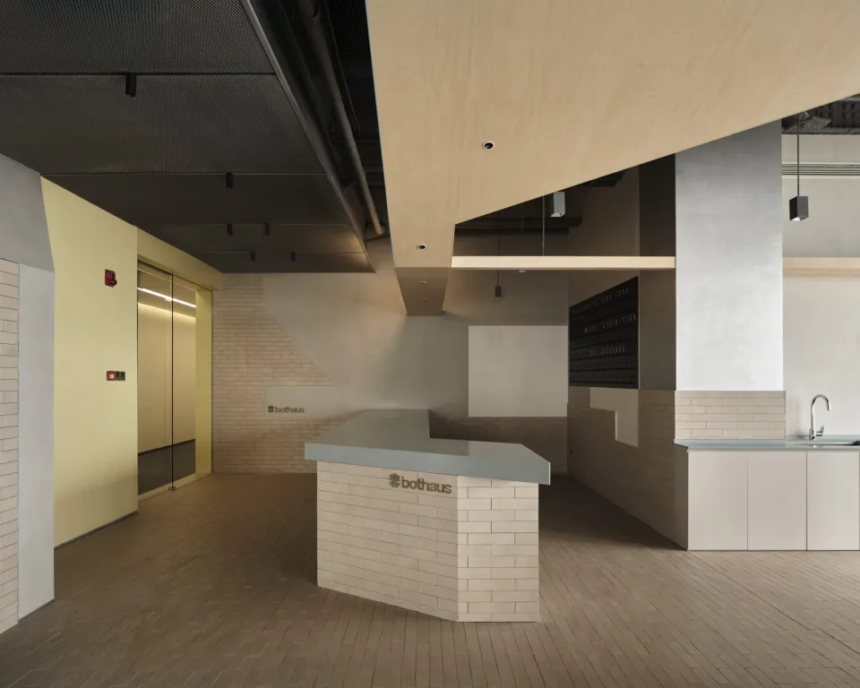 Modern minimalist reception desk made of white brick with a light gray countertop, set in an open commercial interior with birch wood ceiling elements and concrete walls.