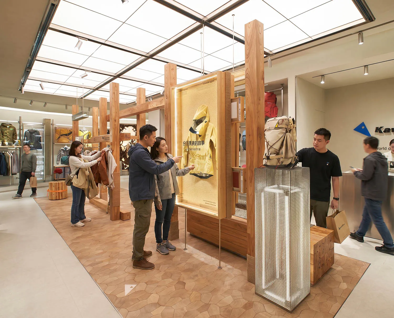 現代戶外用品零售店內部,設有木質結構框架、網狀金屬展示塔,以及顧客正在觀看明亮照明的黃色雨衣展示。