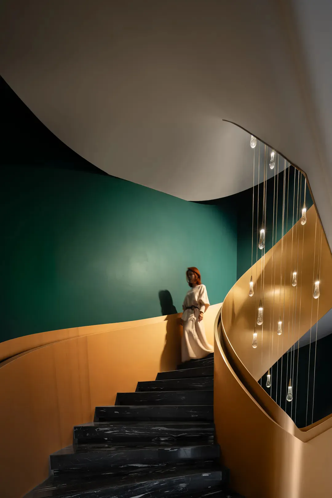 Modern curved black marble staircase with golden handrail, teal accent wall, and multiple hanging glass pendant lights, with a woman in a white dress standing on the steps.