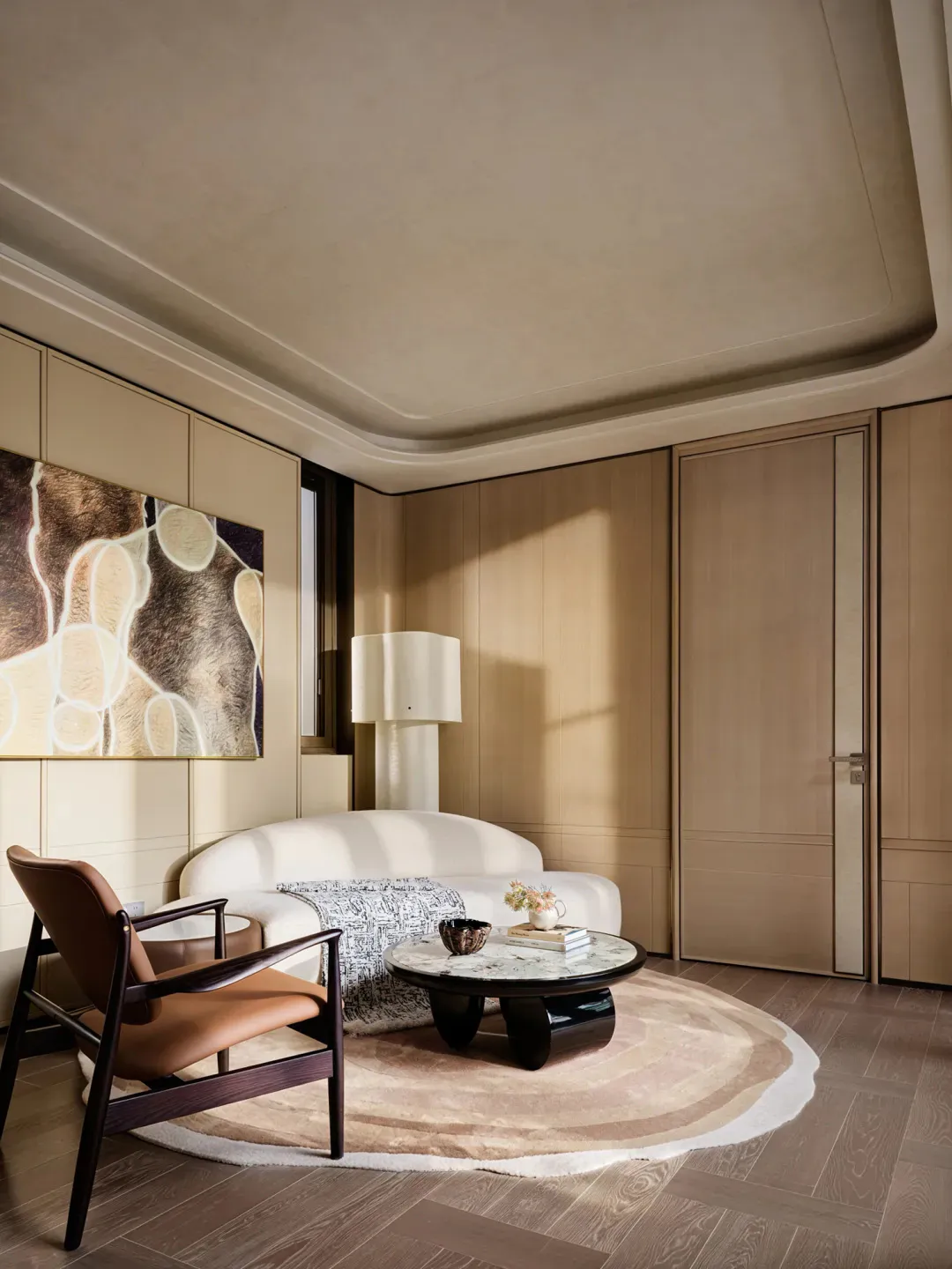 Modern minimalist living room with a curved white sofa, brown leather armchair, round marble coffee table on a circular beige rug, large abstract painting, and warm wood paneling.