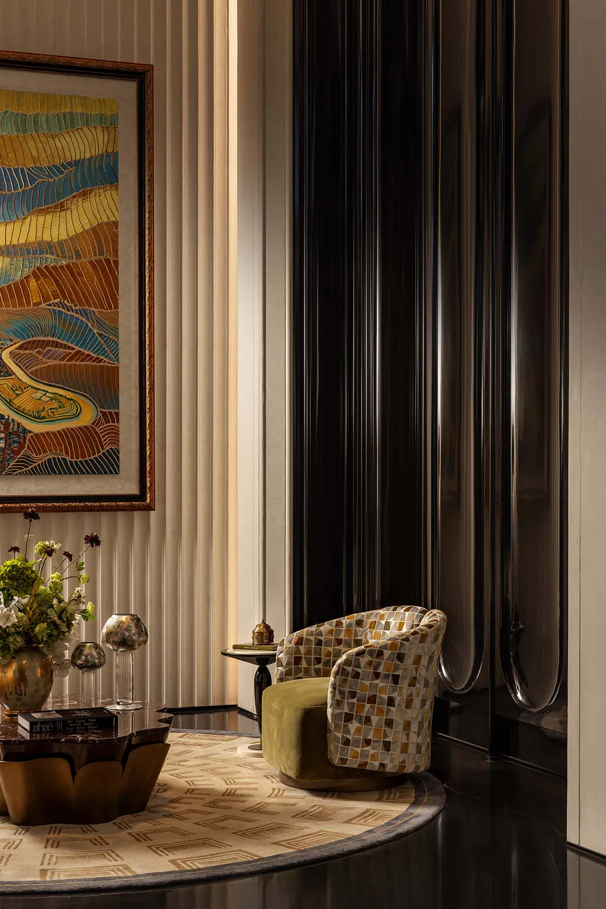 Elegant modern interior corner featuring a green velvet and multicolored mosaic patterned swivel armchair, abstract landscape painting, dark fluted wall panel, and sculptural coffee table on a geometric rug.
