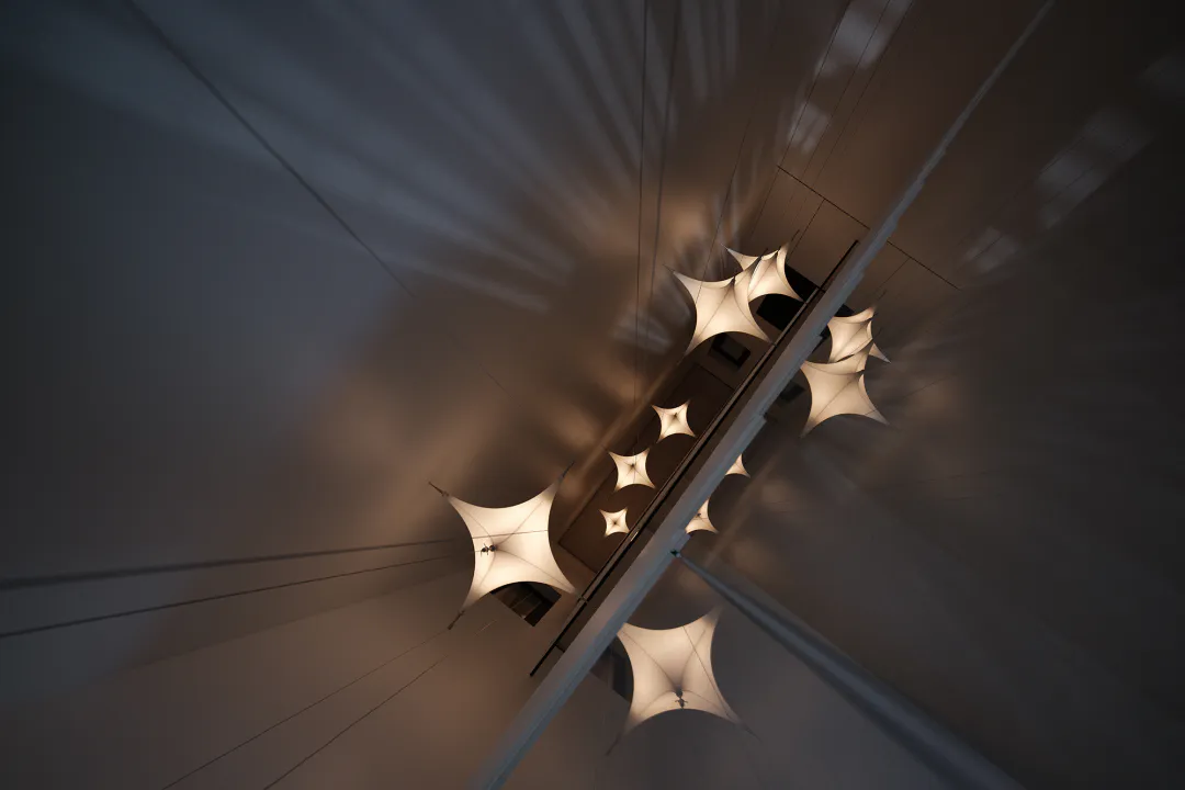 Low-angle view looking up at a series of star-shaped fabric pendant lights suspended over a modern staircase, casting warm light and dramatic shadows on the walls and ceiling.