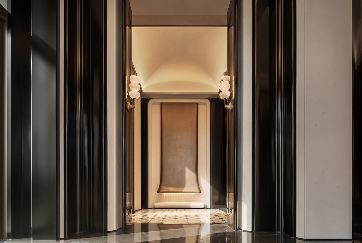 Symmetrical luxury hallway featuring dark fluted marble walls, light stone archway, and matching wall sconces with glowing spherical lights.