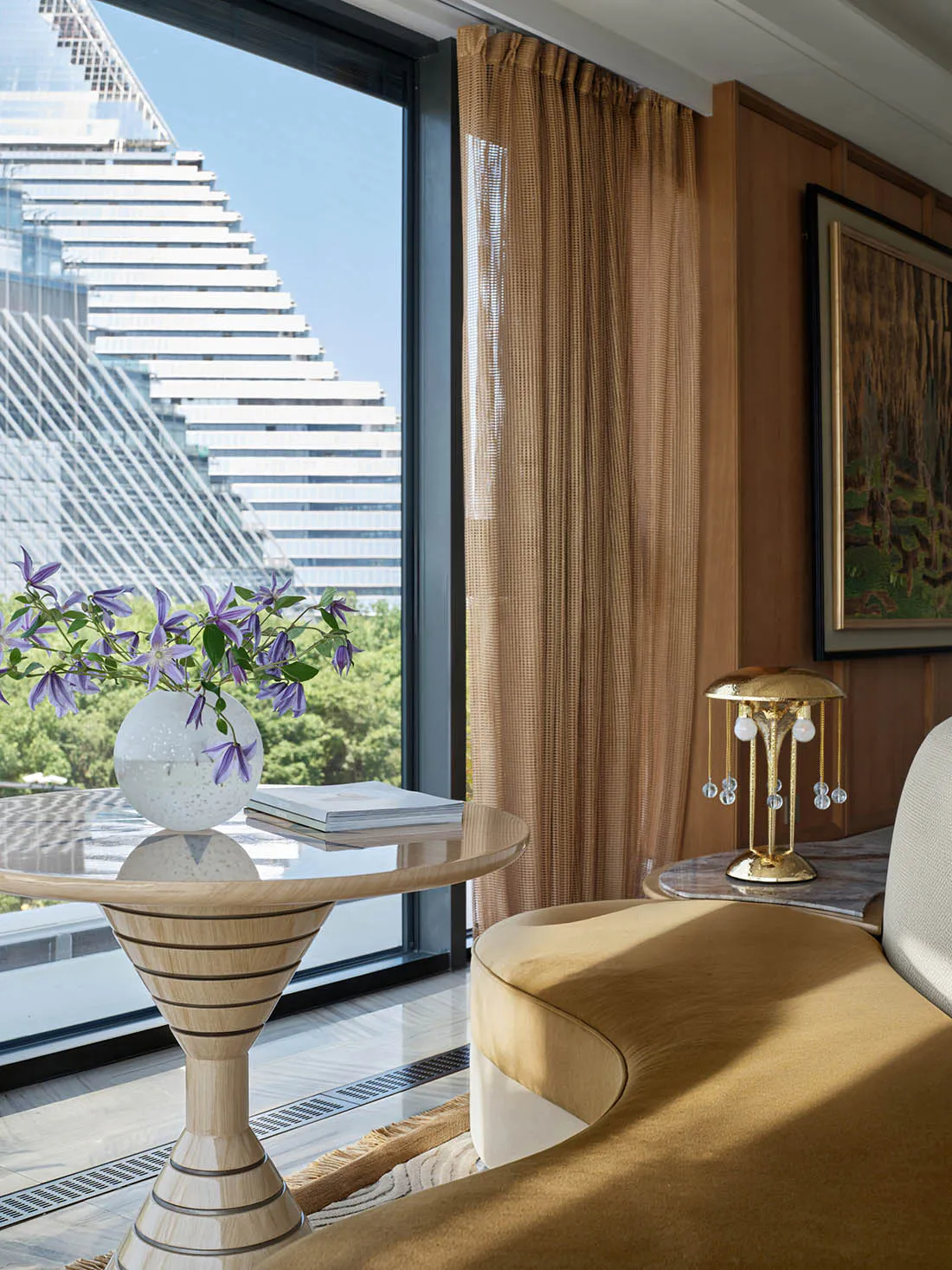 Modern luxury living room interior featuring a sculptural light-wood pedestal table with purple flowers, mustard yellow curved sofa, walnut wall paneling, and a dramatic city skyscraper view through floor-to-ceiling windows.
