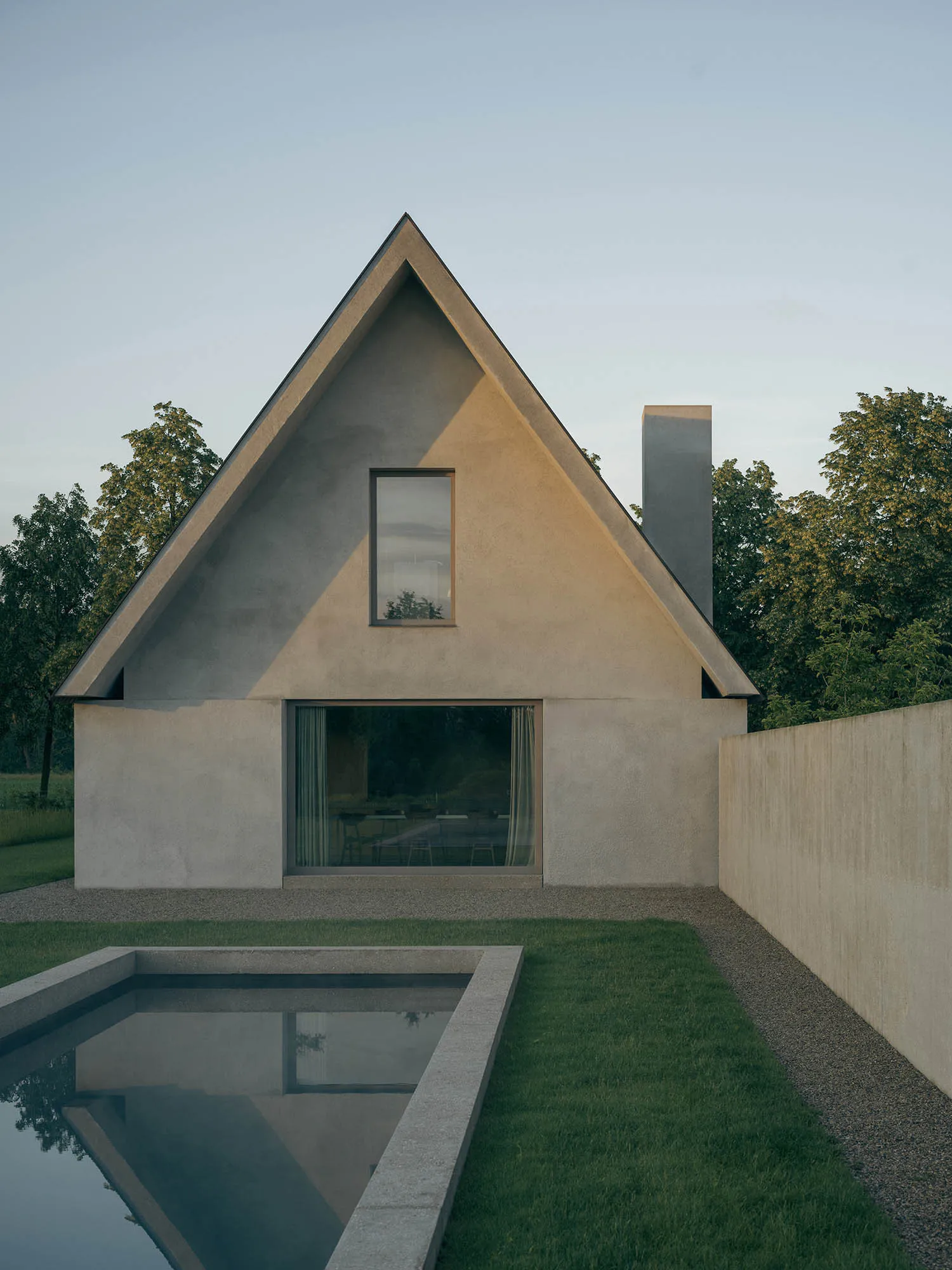 Modern triangular concrete house with a large gable roof, floor-to-ceiling glass windows, and a rectangular reflecting pool in the foreground surrounded by lawn and trees.