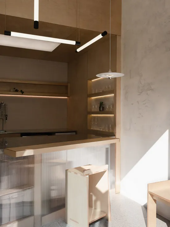 Modern minimalist kitchen corner with a light oak bar counter, fluted glass front, built-in illuminated shelving, and contemporary linear and disc pendant lights.
