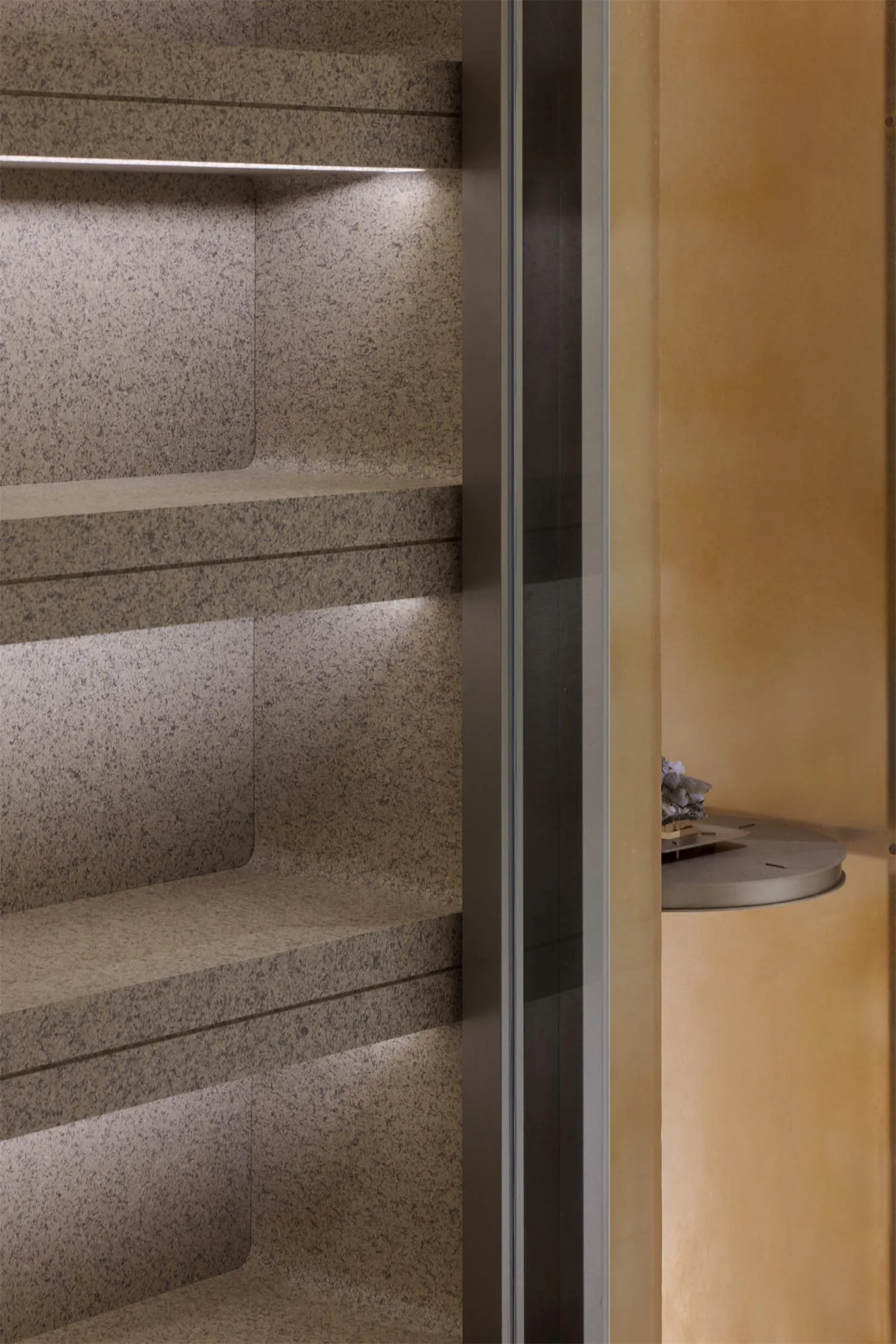 Close-up of built-in terrazzo niche shelves with warm integrated LED strip lighting and a glimpse of a round side table in the background.