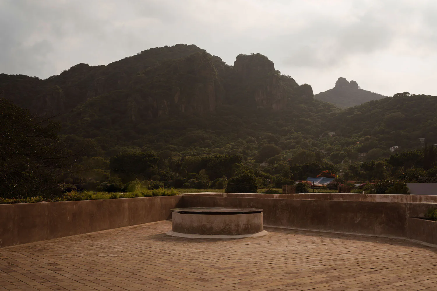 Rooftop terrace with circular concrete feature, brick pavers, and expansive view of forested mountains at dusk