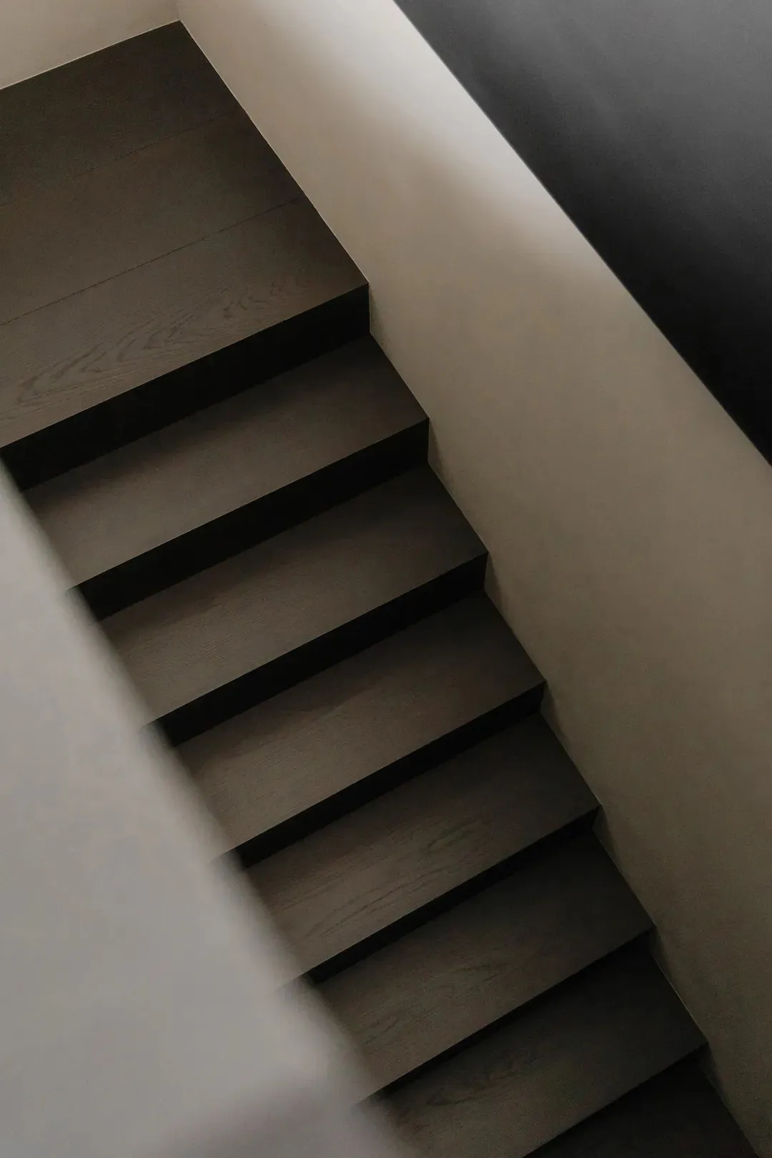 Overhead view of a modern dark oak floating staircase with open risers and concrete walls.