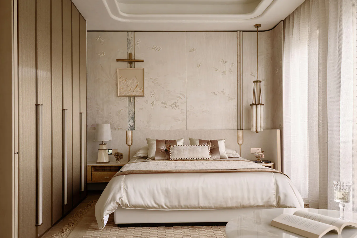 Elegant modern bedroom with a large bed dressed in cream and taupe silk and velvet bedding, embossed floral wallpaper, tall wooden wardrobe, marble side table with open book, and sculptural pendant light.