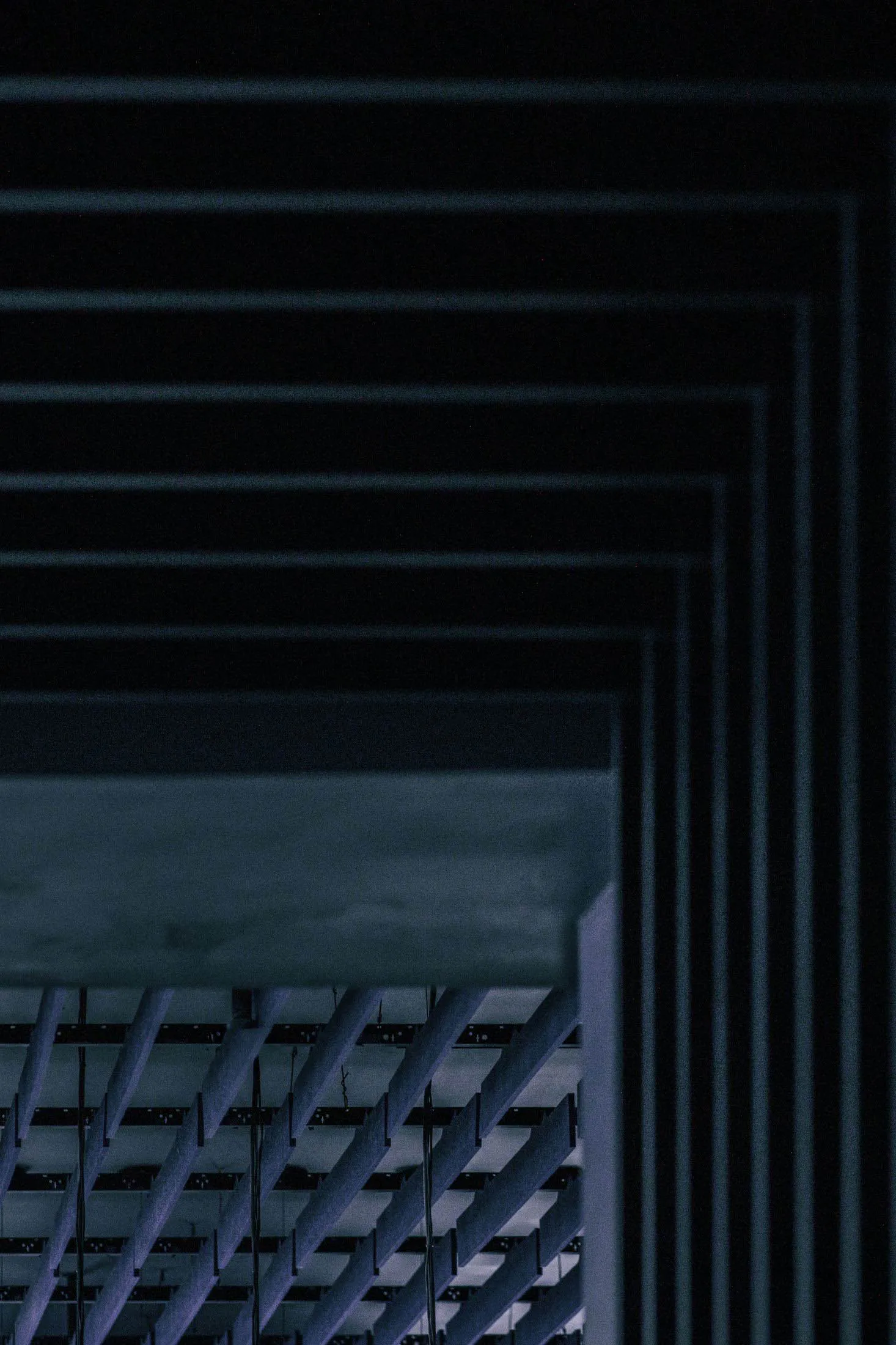 Looking up at a brutalist concrete ceiling featuring parallel cylindrical beams and layered rectangular frames in deep shadow.