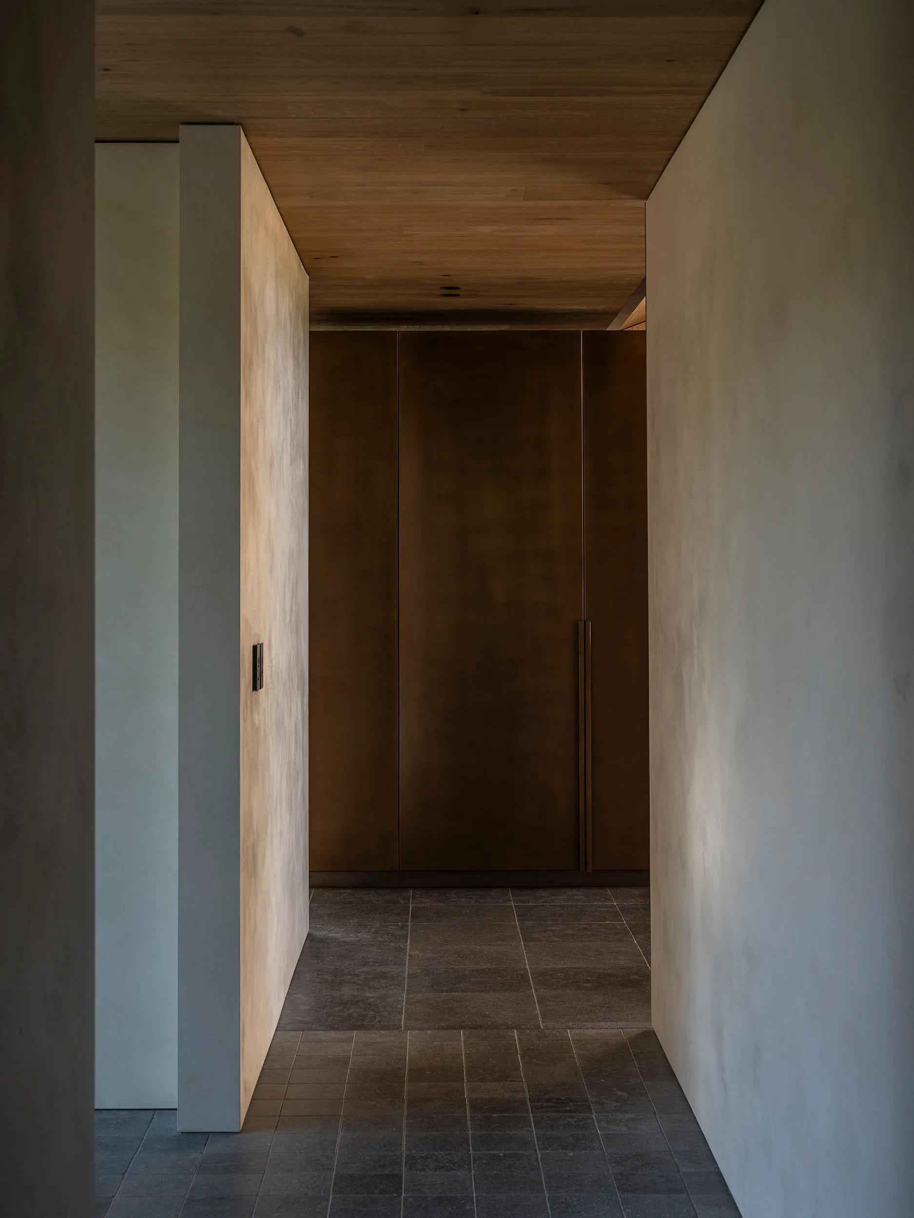 Narrow minimalist hallway featuring concrete walls, dark wood cabinetry, wood plank ceiling, and dark tiled floor.