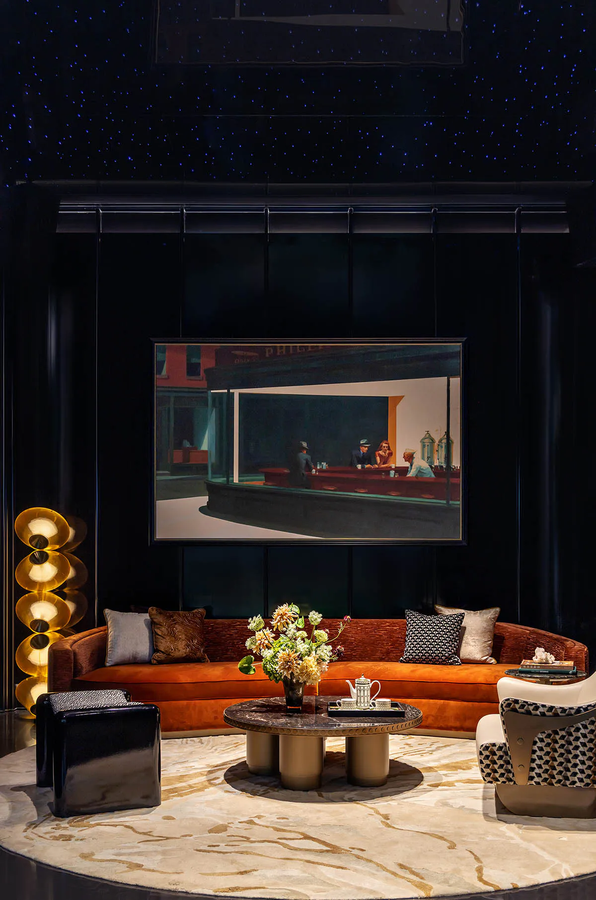 Luxurious modern living room with burnt orange curved velvet sofa, marble coffee table, floral arrangement, black and gold floor lamp, patterned armchair, and a large framed Edward Hopper painting of a diner scene on a dark wall under a starry ceiling.