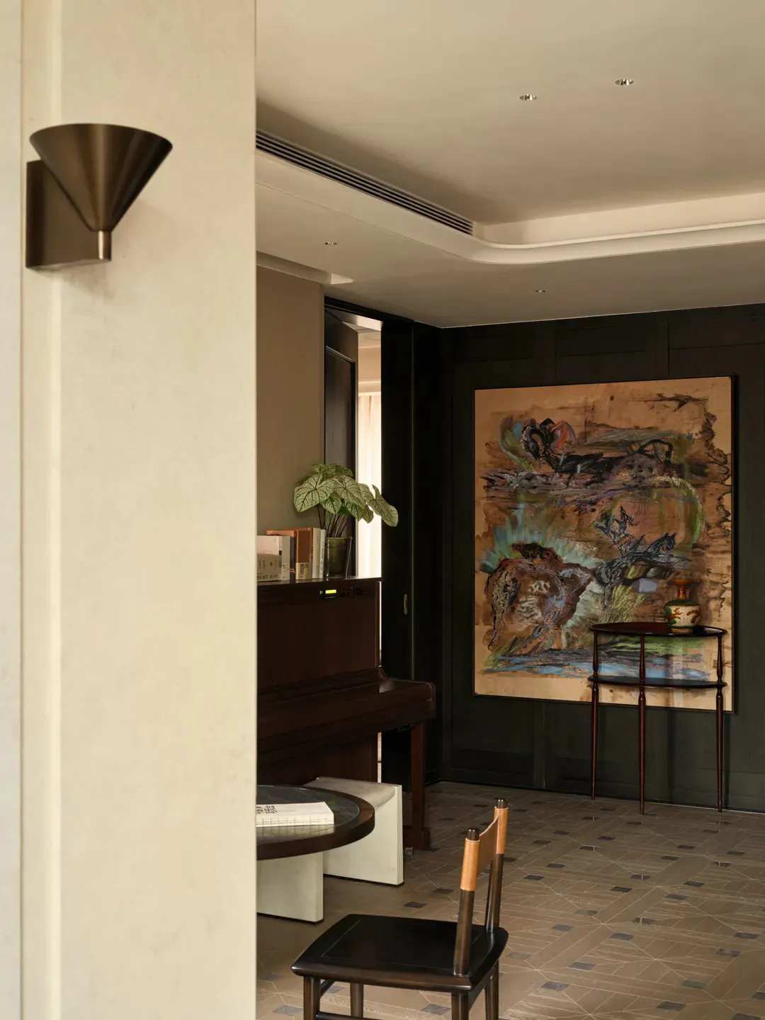 Modern entryway featuring a dark wood upright piano, a large abstract painting, a wooden chair, and a potted plant under warm lighting.