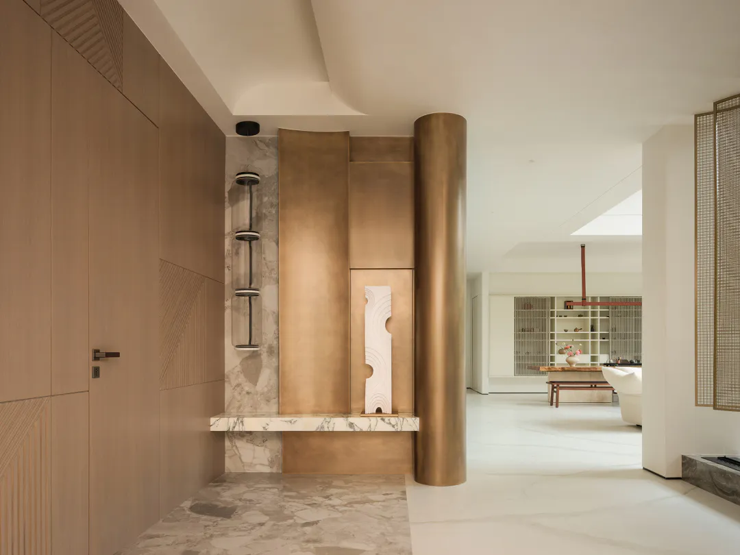 Modern entryway featuring a curved brass feature wall, marble console, cylindrical column, and integrated lighting, leading to a bright open-plan living area.