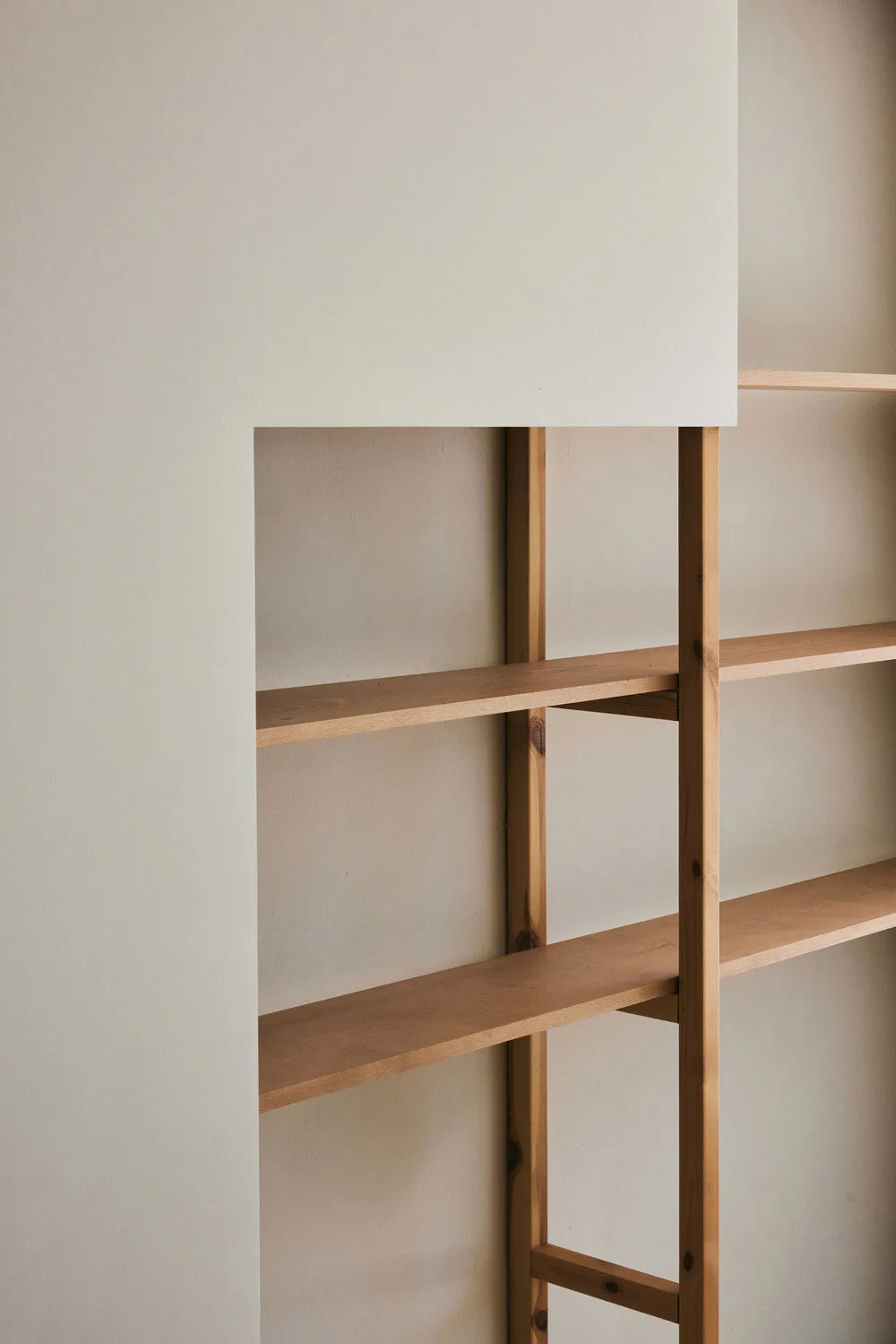Close-up view of a minimalist built-in shelving unit made from light-colored solid wood set into a white wall niche.
