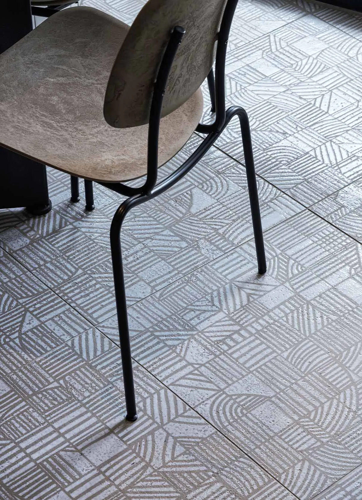 Black metal chair with a curved back and upholstered seat positioned on a grey and white geometric patterned terrazzo tile floor.