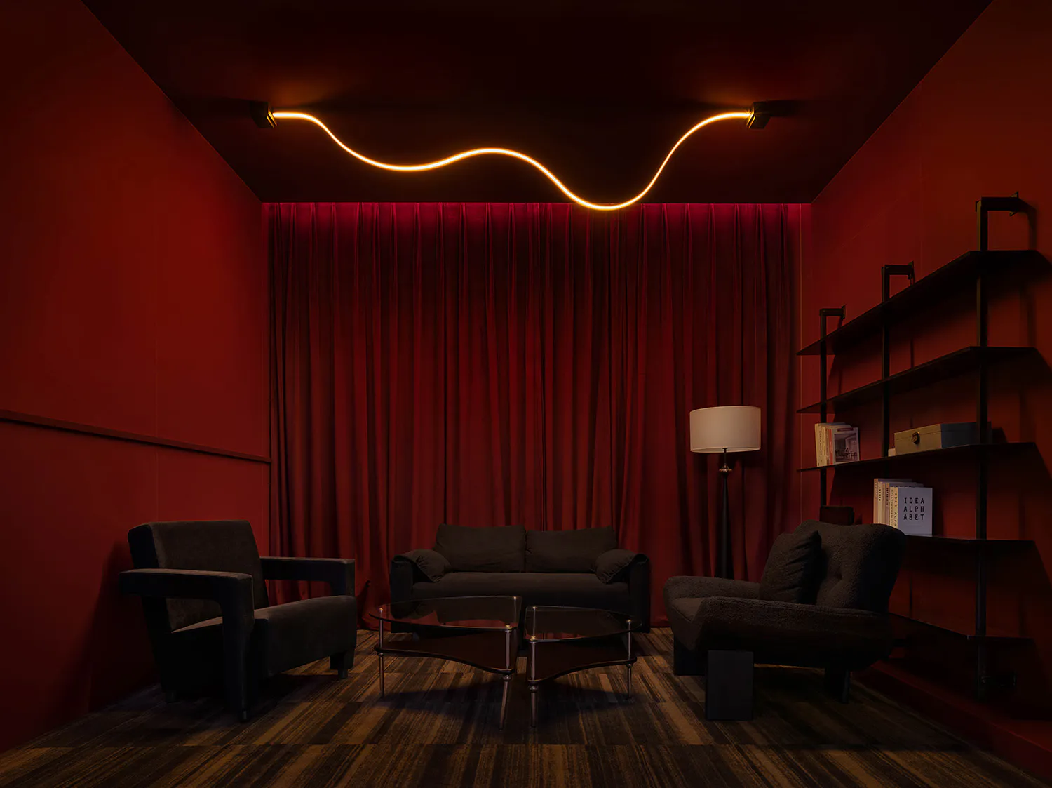 Dark red home theater room featuring black velvet sofas and armchairs, a wavy orange LED light strip on the ceiling, and heavy red velvet curtains.