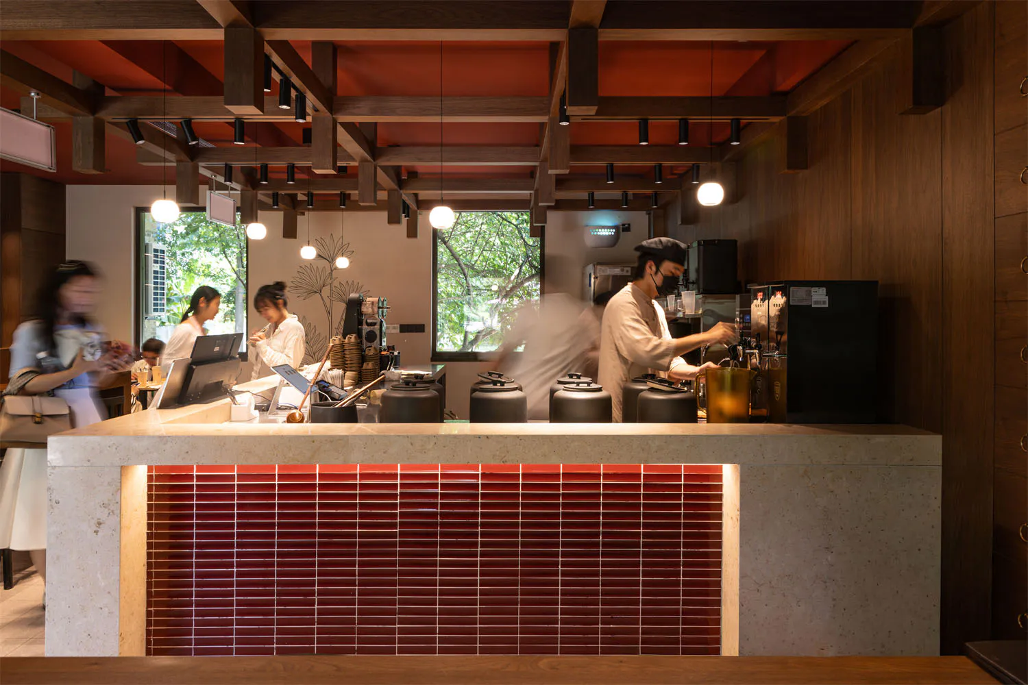 Modern cafe interior featuring a terrazzo counter with red tiled front, warm wood elements, and staff preparing drinks.
