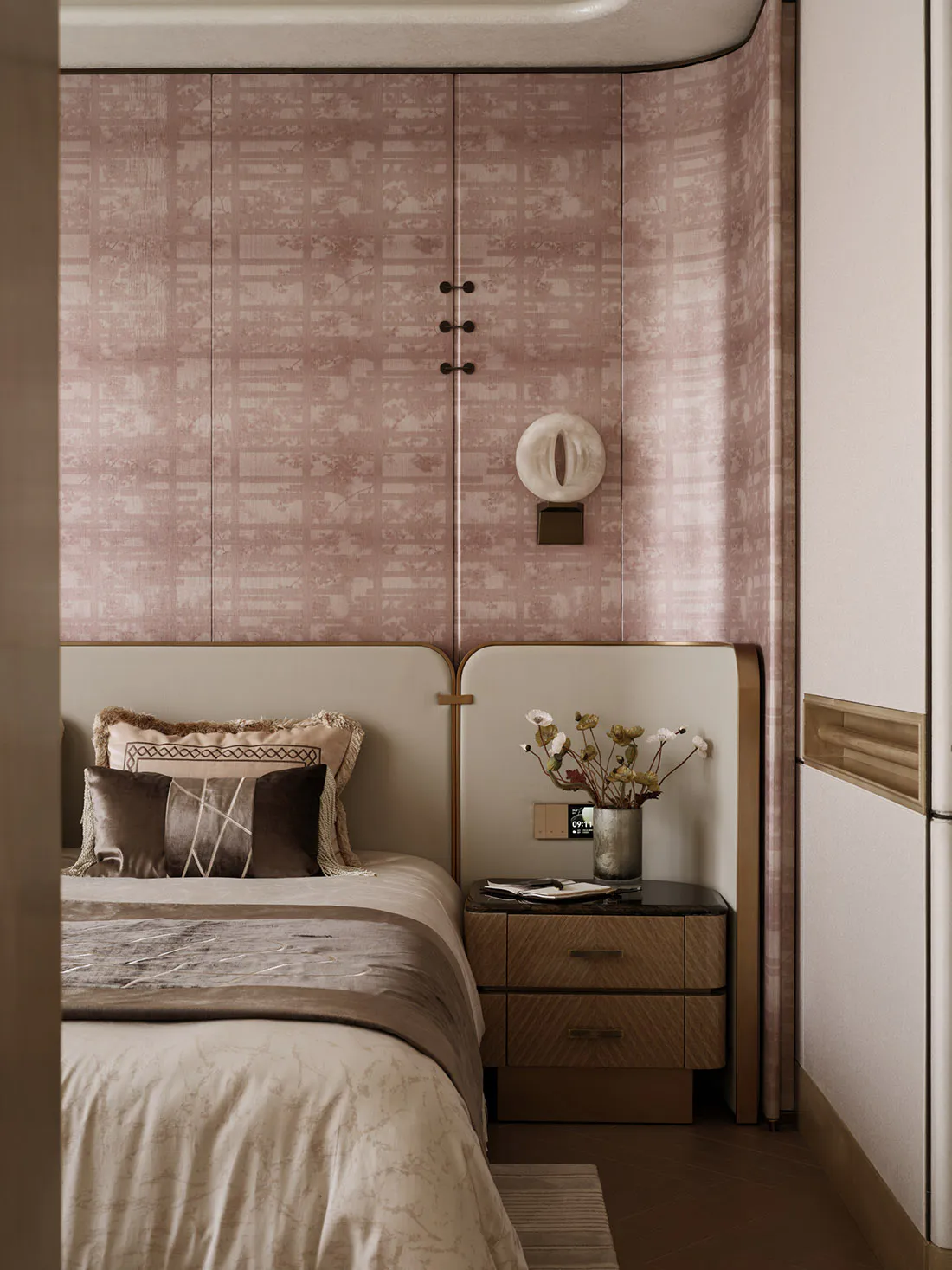 Modern luxury bedroom interior with pinkish-taupe patterned wallpaper, curved architectural wall, upholstered headboard, walnut nightstand, and decorative wall sconce.