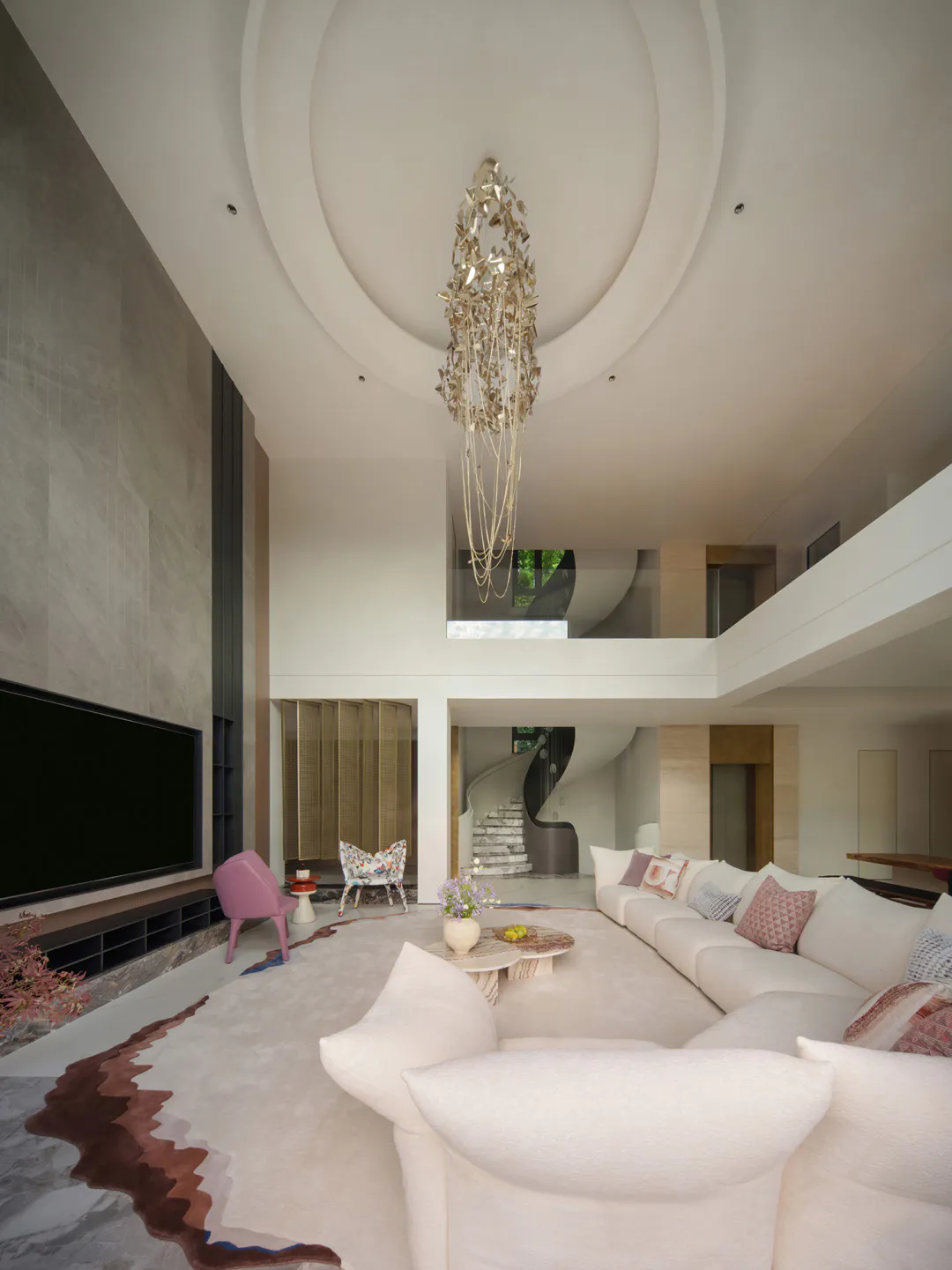 Modern luxury living room with double-height ceiling, large white sectional sofa, pink accent chair, gold statement chandelier, and marble floor with custom rug.