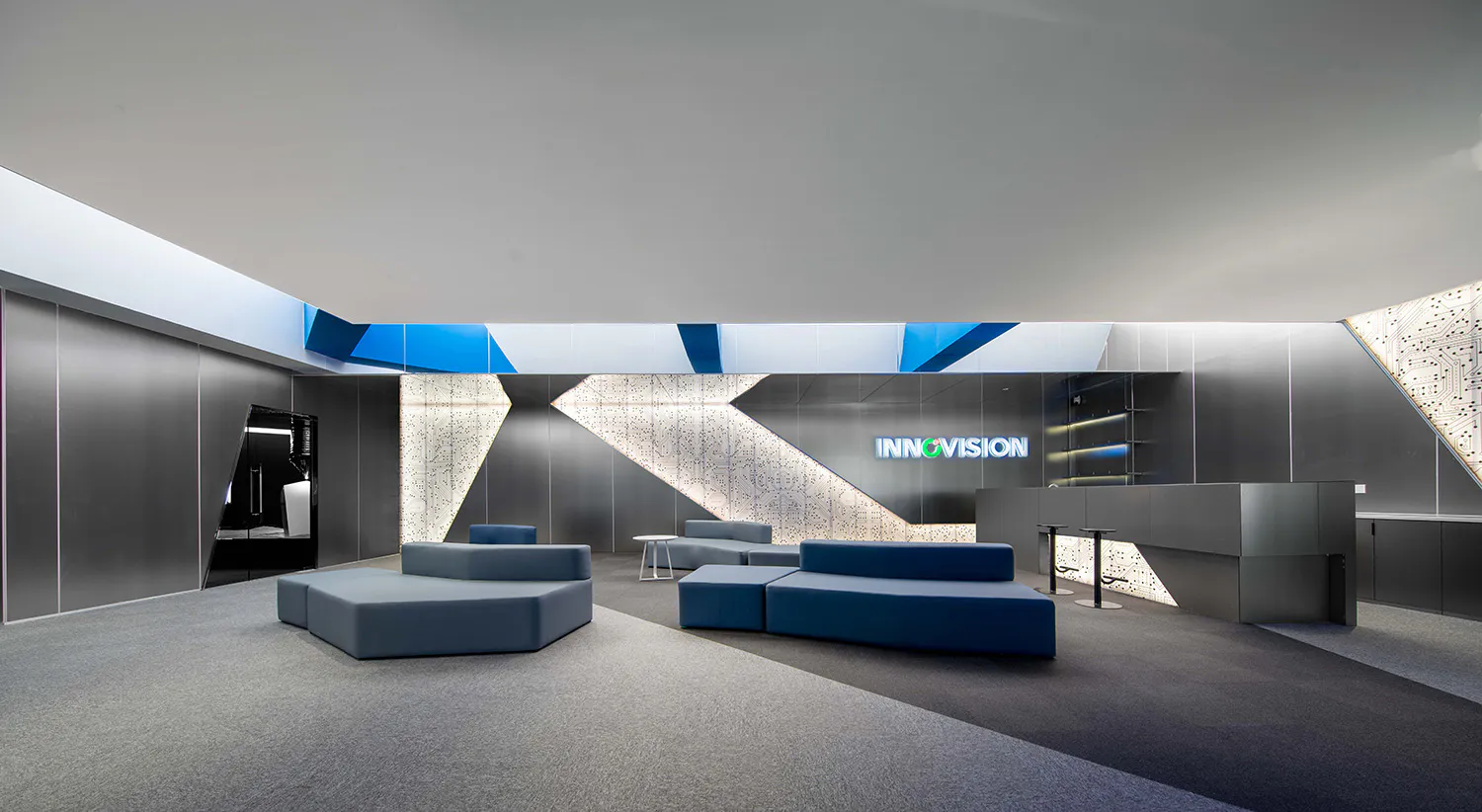Modern corporate lobby interior with blue modular sofas, geometric lighting features, and a large illuminated INNOVISION logo on a dark wall with circuit board patterns.