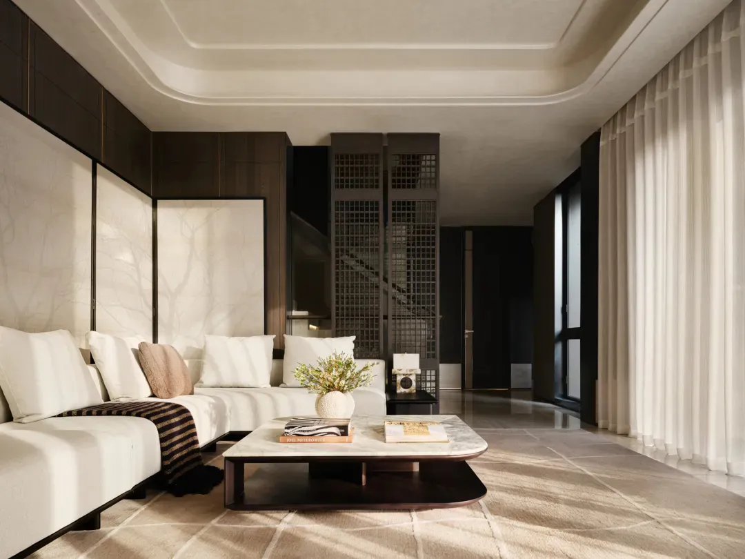 Modern luxury living room featuring a white L-shaped sectional sofa, marble coffee table with books and a floral arrangement, dark wood wall paneling with marble inlay, and a dramatic grid-patterned room divider leading to a staircase.