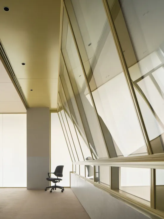 Empty modern executive office featuring floor-to-ceiling brass mullion windows, a single black office chair, and soft natural light.