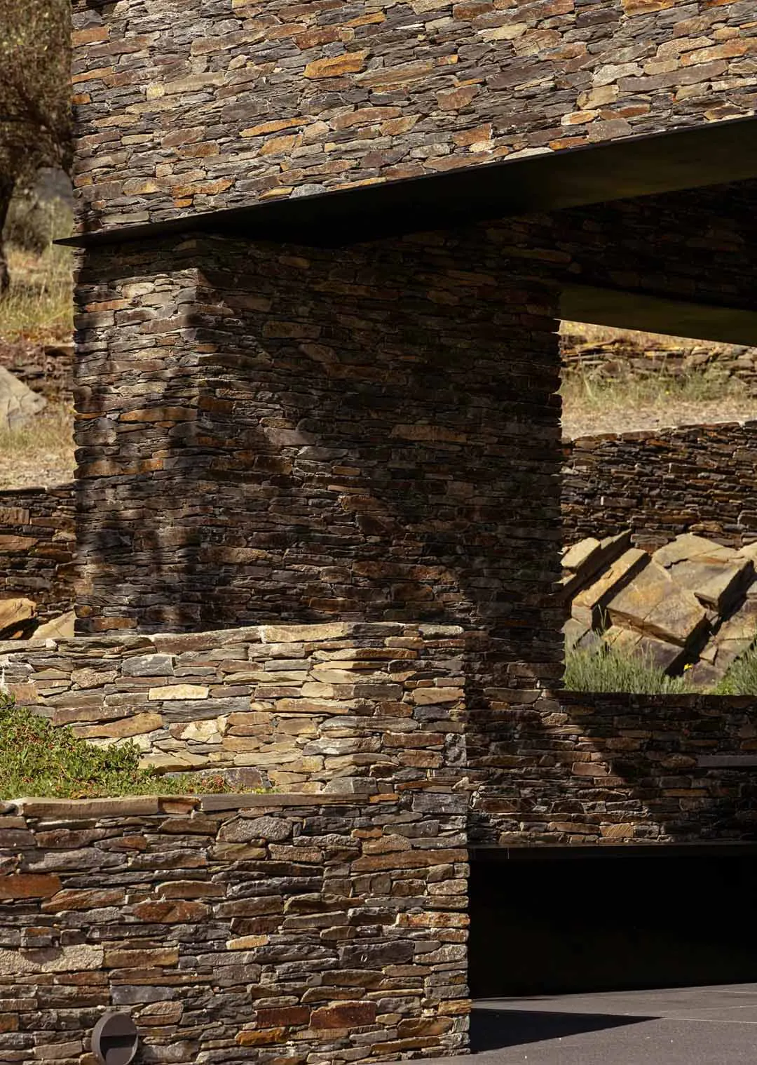 Close-up view of a rustic natural stone pillar and horizontal overhang with textured masonry walls under bright sunlight.