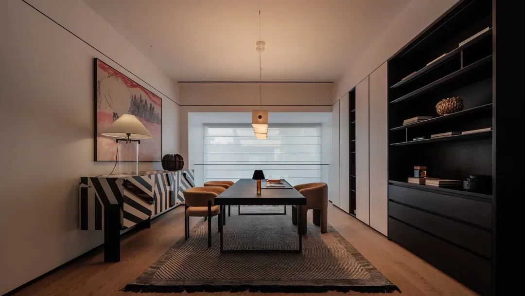 Modern minimalist dining room with dark wood dining table, four upholstered chairs, large black bookshelf, zebra-pattern console table with lamp and artwork, pendant light, and large window with blinds.