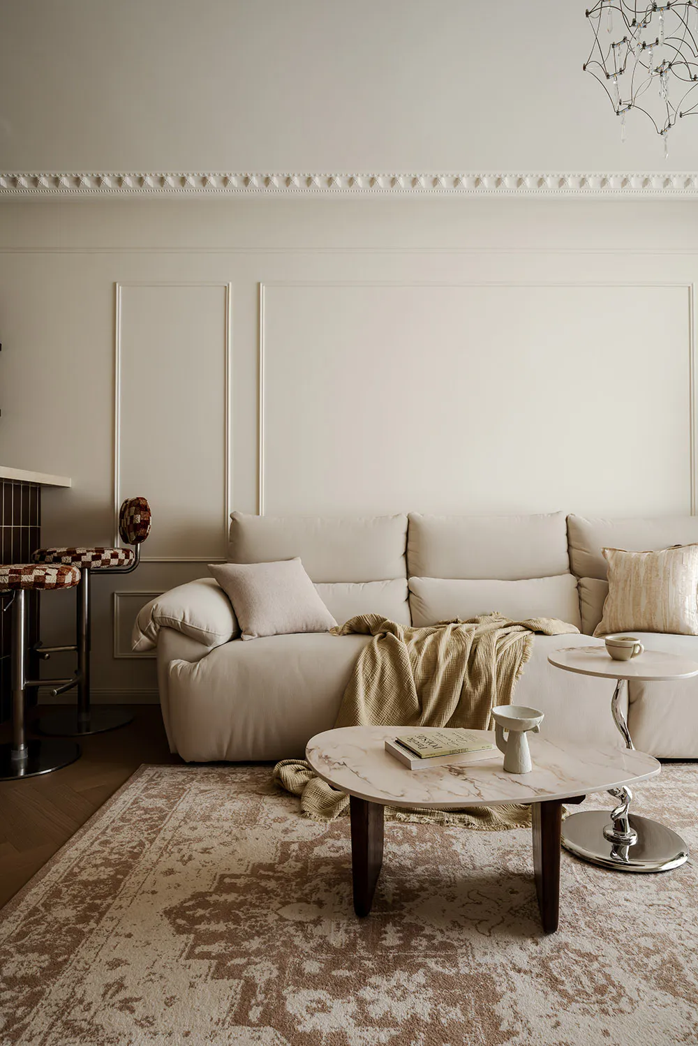 Modern neutral living room with a large off-white sectional sofa, round marble coffee table, patterned area rug, and decorative crown molding on the wall.
