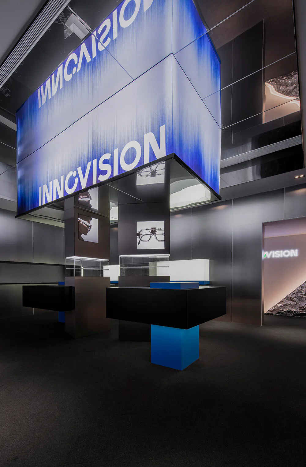 Modern eyewear retail store interior featuring a large suspended blue LED cube with 'INNOVISION' branding, illuminated glass display cases, and minimalist black and blue furniture.