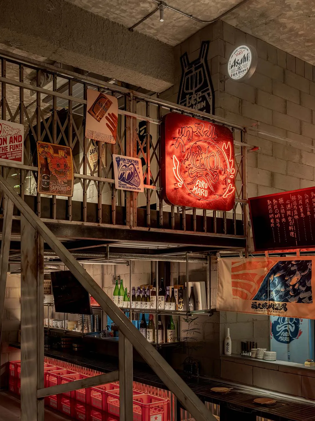 Multi-level industrial Japanese izakaya interior featuring red neon Oni mask sign, metal railings, concrete block walls, and shelves filled with sake bottles.